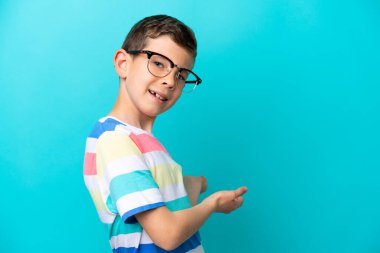 Little boy isolated on blue background With glasses and presenting something
