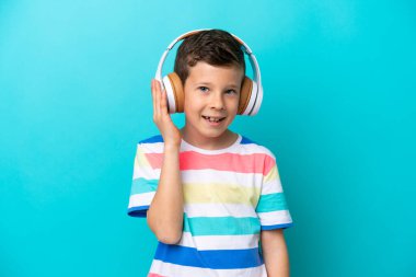 Küçük çocuk mavi arka planda izole edilmiş müzik dinliyor.
