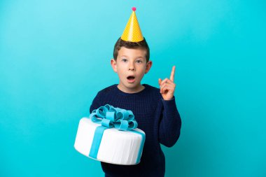 Little boy holding birthday cake isolated on blue background thinking an idea pointing the finger up