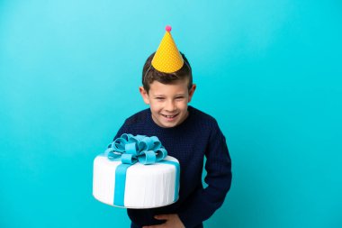 Mavi arka planda izole edilmiş doğum günü pastası tutan küçük çocuk çok gülümsüyor.