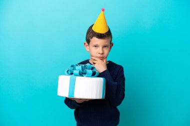 Little boy holding birthday cake isolated on blue background thinking