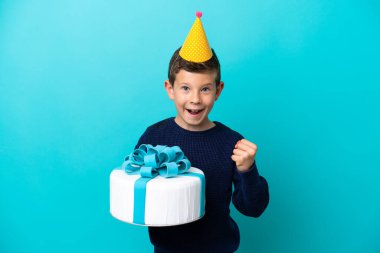Little boy holding birthday cake isolated on blue background celebrating a victory in winner position