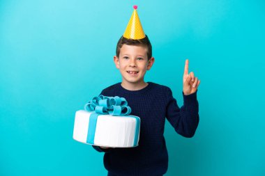 Mavi arka planda izole edilmiş doğum günü pastası tutan küçük çocuk harika bir fikre işaret ediyor.