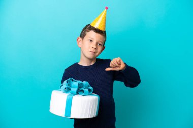 Little boy holding birthday cake isolated on blue background proud and self-satisfied