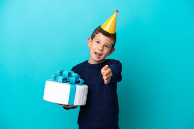 Little boy holding birthday cake isolated on blue background shaking hands for closing a good deal