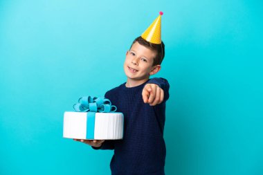 Little boy holding birthday cake isolated on blue background pointing front with happy expression