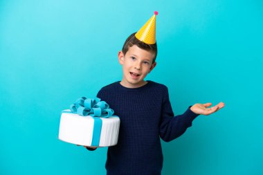 Little boy holding birthday cake isolated on blue background with shocked facial expression