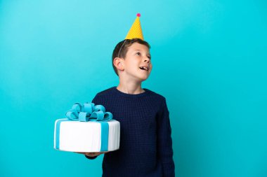 Küçük çocuk mavi arka planda izole edilmiş doğum günü pastası tutuyor.
