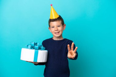 Little boy holding birthday cake isolated on blue background happy and counting three with fingers