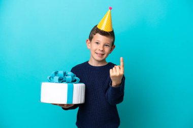 Little boy holding birthday cake isolated on blue background doing coming gesture