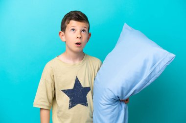 Little boy in pajamas isolated on blue background looking up and with surprised expression