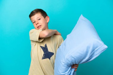 Little boy in pajamas isolated on blue background suffering from pain in shoulder for having made an effort