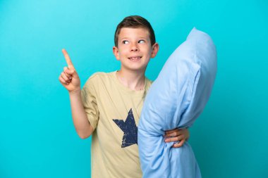 Little boy in pajamas isolated on blue background showing and lifting a finger in sign of the best