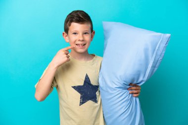 Mavi arka planda izole edilmiş pijamalı küçük bir çocuk baş parmak hareketi yapıyor.