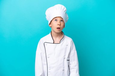Little chef boy isolated on blue background looking up and with surprised expression