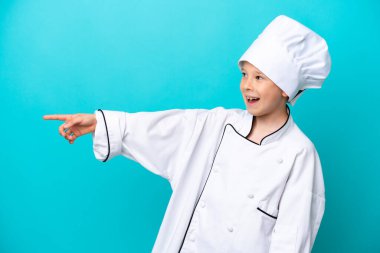 Little chef boy isolated on blue background pointing finger to the side and presenting a product