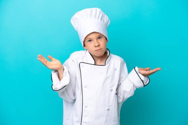Little chef boy isolated on blue background having doubts while raising hands