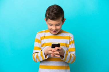 Küçük çocuk mavi arkaplanda izole edilmiş. Cep telefonuyla bir mesaj ya da e-posta gönderiyor.