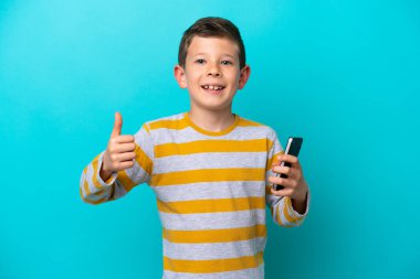 Küçük çocuk mavi arka planda izole edilmiş. Baş parmak kullanırken cep telefonu kullanıyor.