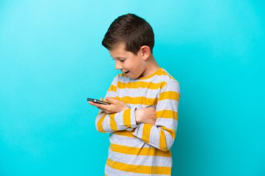 Little boy isolated on blue background holding a mobile phone and with arms crossed