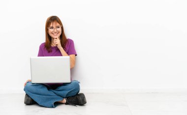 redhead girl with a laptop sitting on the floor looking to the side and smiling