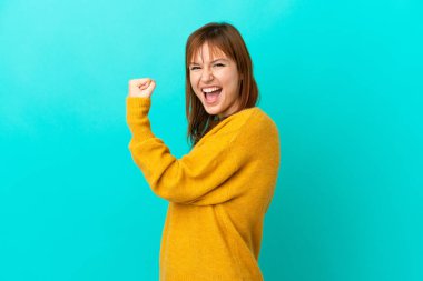 Mavi arka planda izole edilmiş kızıl saçlı kız zaferi kutluyor.