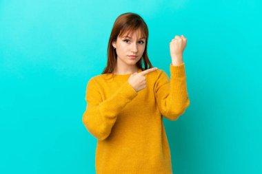 Kızıl saçlı kız mavi arka planda izole edilmiş, geç kalma hareketi yapıyor.