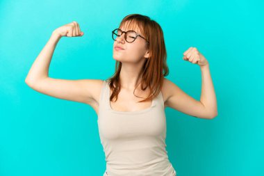 Redhead girl isolated on blue background doing strong gesture