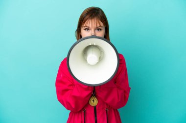 Redhead girl with medals isolated o blue background shouting through a megaphone