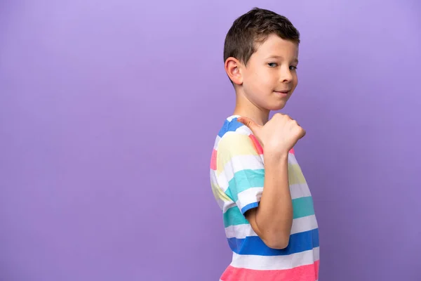 一个被紫色背景隔离的小男孩指着侧面展示了一种产品 — 图库照片