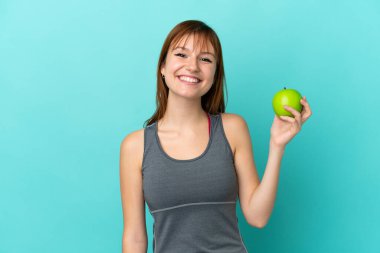 Redhead girl isolated on blue background with an apple and happy