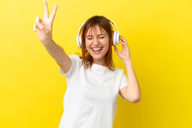 Kızıl saçlı kız sarı arka planda izole edilmiş müzik dinliyor ve şarkı söylüyor.