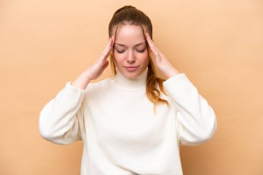 Kafkasyalı genç bir kadın bej arka planda izole edilmiş, baş ağrısı var.