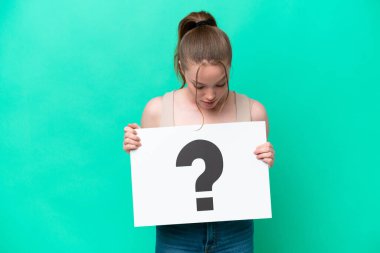 Young caucasian woman isolated on green background holding a placard with question mark symbol