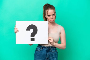 Young caucasian woman isolated on green background holding a placard with question mark symbol with sad expression