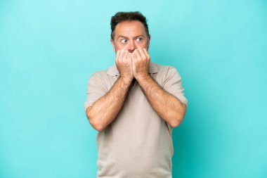 Orta yaşlı beyaz bir adam mavi arka planda izole edilmiş gergin ve korkmuş bir şekilde elleriyle suni teneffüs yapıyor.