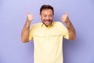 Mor arka planda izole edilmiş orta yaşlı beyaz bir adam baş parmak hareketi yapıyor.