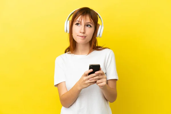 Redhead Girl Isolated Yellow Background Listening Music Mobile Thinking —  Fotos de Stock