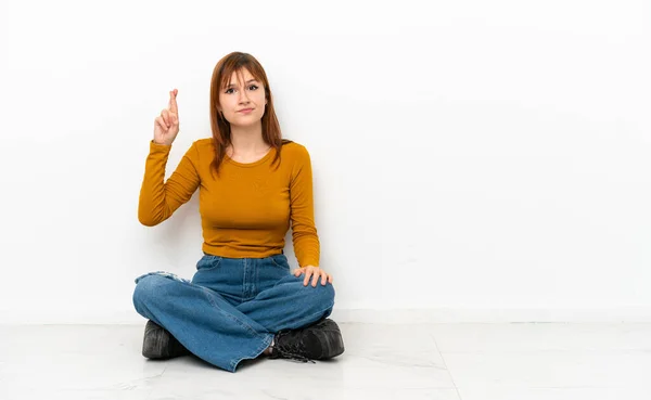 Redhead Girl Sitting Floor Isolated White Background Fingers Crossing Wishing — Stockfoto