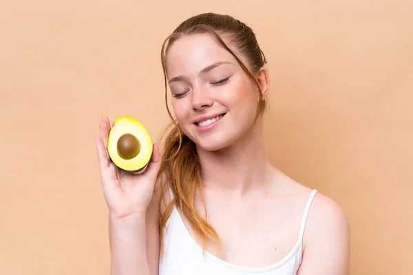 Young Caucasian Girl Isolated Beige Background Holding Avocado While Smiling — Stockfoto