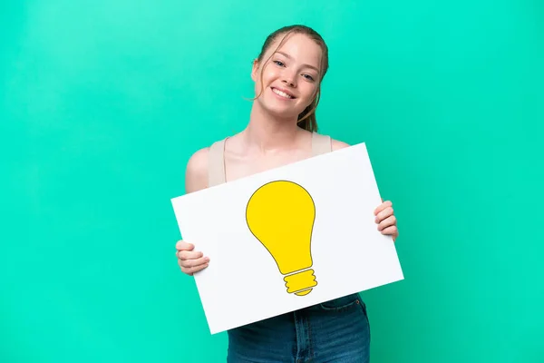 Young Caucasian Woman Isolated Green Background Holding Placard Bulb Icon — Stockfoto