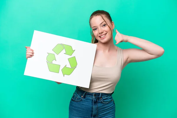 Young caucasian woman isolated on green background holding a placard with recycle icon and doing phone gesture