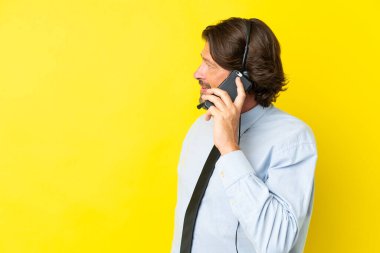 Tele pazarlamacı Hollandalı adam sarı arka planda izole edilmiş bir kulaklıkla çalışıyor cep telefonuyla biriyle sohbet ediyor.