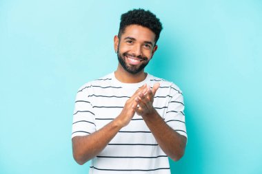 Mavi arka planda izole edilmiş genç Brezilyalı bir adam bir konferanstan sonra alkışlıyor.