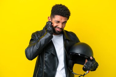 Motosiklet kasklı genç Brezilyalı adam sarı arka planda izole edilmiş hayal kırıklığına uğramış ve kulaklarını kapatmış.