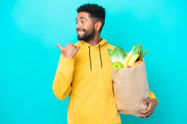 Genç Brezilyalı bir adam mavi arka planda izole edilmiş bir paket yiyecek alıyor.