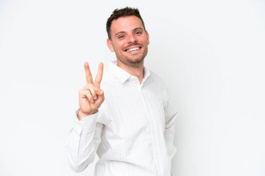 Beyaz arka planda izole edilmiş beyaz tenli yakışıklı adam gülümsüyor ve zafer işareti gösteriyor.