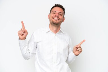 Beyaz arka planda izole edilmiş beyaz tenli yakışıklı adam parmak uçlarını işaret ediyor ve mutlu.