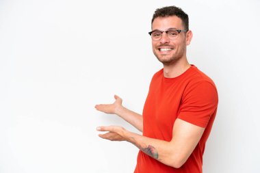 Beyaz arka planda soyutlanmış beyaz tenli yakışıklı adam, davet edilmek için ellerini yana uzatıyor.