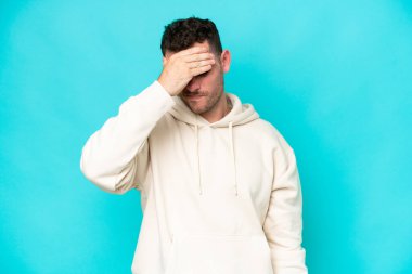 Kafkasyalı yakışıklı genç adam mavi arka planda başağrısı ile izole edilmiş.